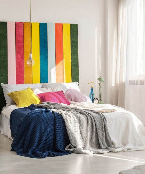 Green, pink, red, orange, yellow and blue bedhead behind king size bed with pillows and blankets; Shutterstock ID 1524660443; purchase_order: -; job: -; client: -; other: -